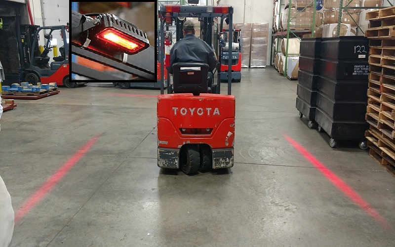 A Toyota forklift operator using a red light at a warehousing place to warn other workers where the safety distance is.